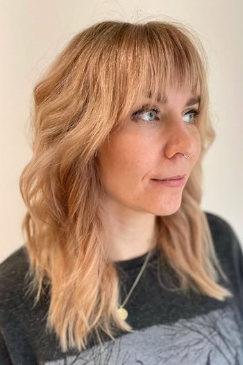 Textured Medium-Length Shag with Bangs Haircut on a woman with blonde hair.