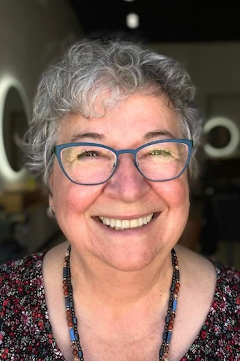 Curly Silver Pixie Hairstyle on a woman in her 60s wearing glasses.