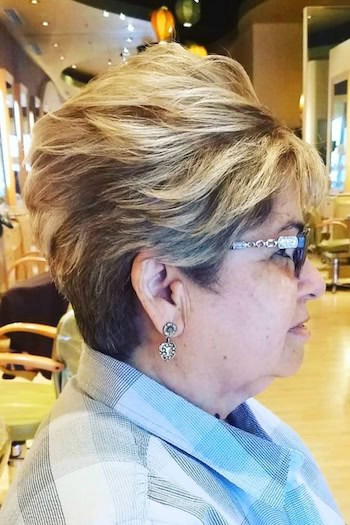 Voluminous Layered Pixie With Blonde Highlights Hairstyle on a woman in her 60s wearing glasses, side view.