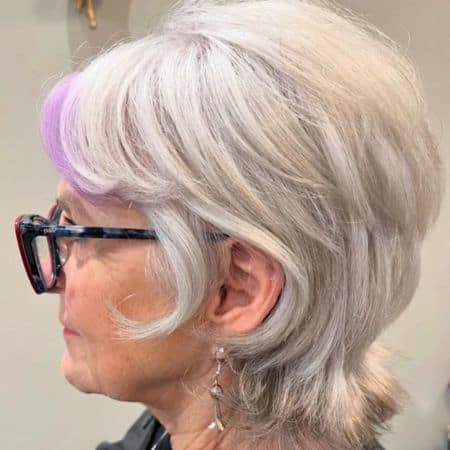 Silver Stacked Pixie Mullet With Purple Accent Hairstyle on a woman in her 60s wearing glasses, side view.