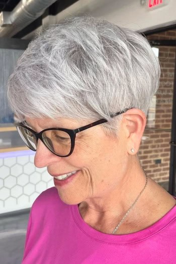 Rounded Silver Pixie Hairstyle on a woman in her 60s wearing glasses.