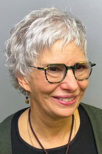Short Wavy Silver Pixie Hairstyle on a woman in her 60s wearing glasses.