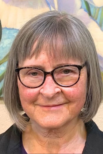 Gray Bob With Bangs Hairstyle on a woman in her 60s wearing glasses.