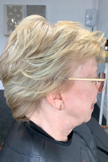 Short Blonde Layers Hairstyle on a woman in her 60s wearing glasses, side view.