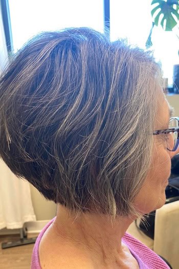 Stacked Gray Bob Hairstyle on a woman in her 60s wearing glasses, side view.