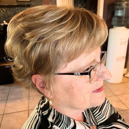 Cropped Layers With Bangs Hairstyle on a woman in her 60s wearing glasses.
