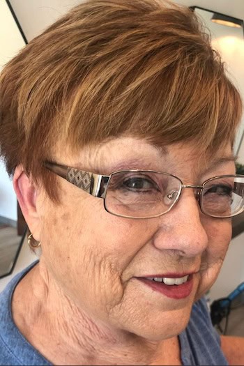Textured Brunette Pixie Hairstyle on a woman in her 60s wearing glasses.