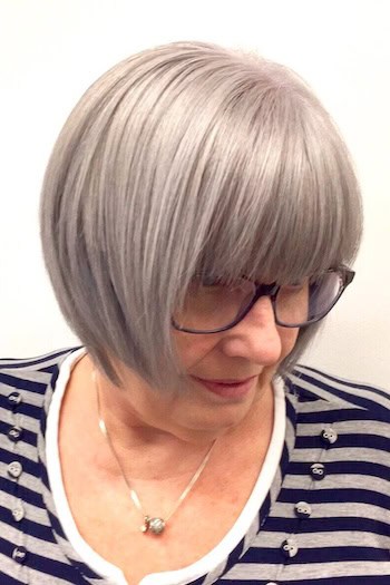 Cropped Gray Bob With Full Bangs Hairstyle on a woman in her 60s wearing glasses.
