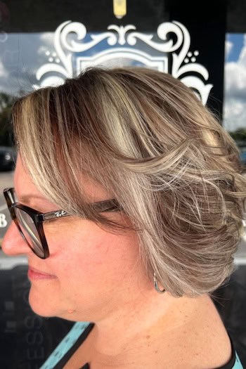 Wavy Highlighted Bob With Layers Hairstyle on a woman in her 60s wearing glasses, side view.