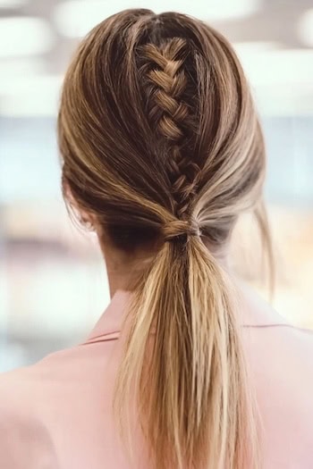 Elegant low ponytail featuring a stylish middle braid for a sophisticated look.